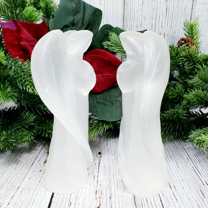 Two large selenite angels facing each otehr with christmas greenery in background